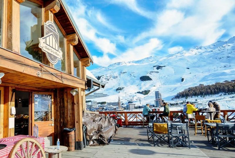 A sunny restaurant deck with snowy slopes behind