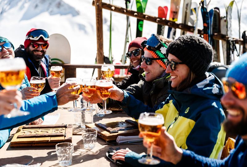 A group of freidns cheers with beers, wearing sunglasses sat outside on a terrace