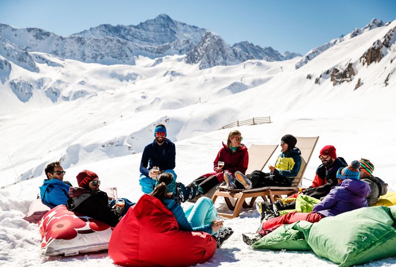 A group of friends sit around on deck chairs and beanbags on the snow on the mountain