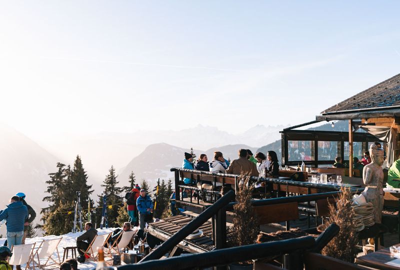 An outdoor terrace for apres ski has a few people seated under the late-day sun