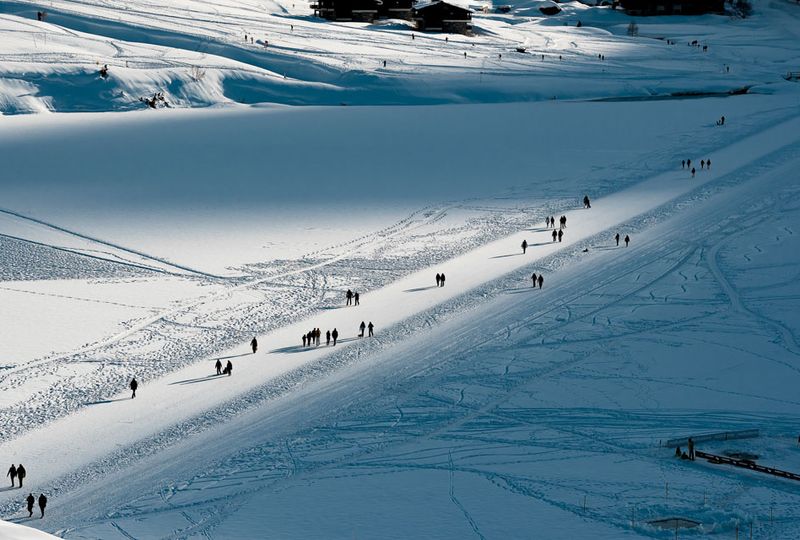 A snowy pathway is dotted with people in this photo taken from above