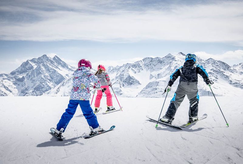 Young skiers in St Anton at what looks like the top of the resort, pushing off onto a slope with a very dramatic, white mountain backdrop