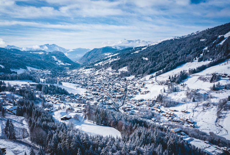 a snow covered village is shot from afar (and above), the snow covered roofs looking pretty in a long valley covered in snow