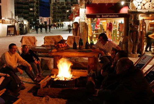Friends sit around a firepit in town at night time, outside a restaurant