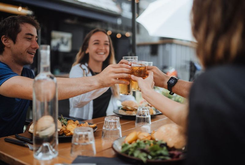 Four hands clink beer glasses at a restaurant table with burgers