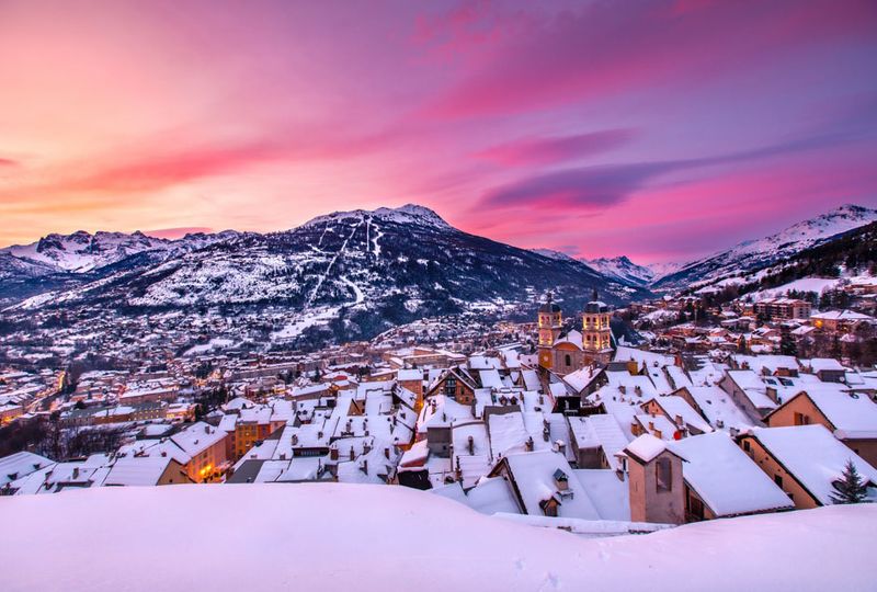 A snowy alpine village under a blanket of snow and pink sky
