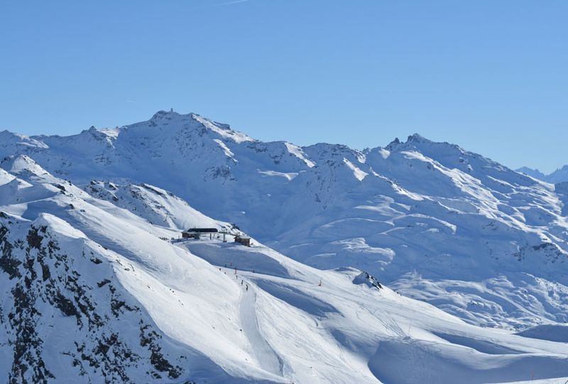 A beautiful mountainscape with huge, white mountains in the background, a lift station visible surrounded by very snowy slopes