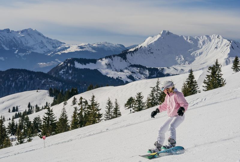 a snowboarder in pink makes their way down a piste, with a majestic mountain backdrop