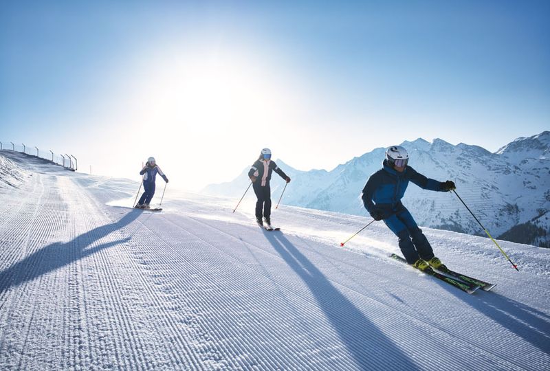 Three skiers in a line head down a mellow corduroy piste